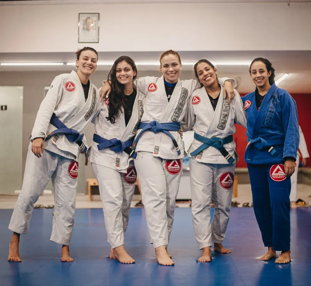 Alunas da turma feminina abraçadas e sorrindo no tatame