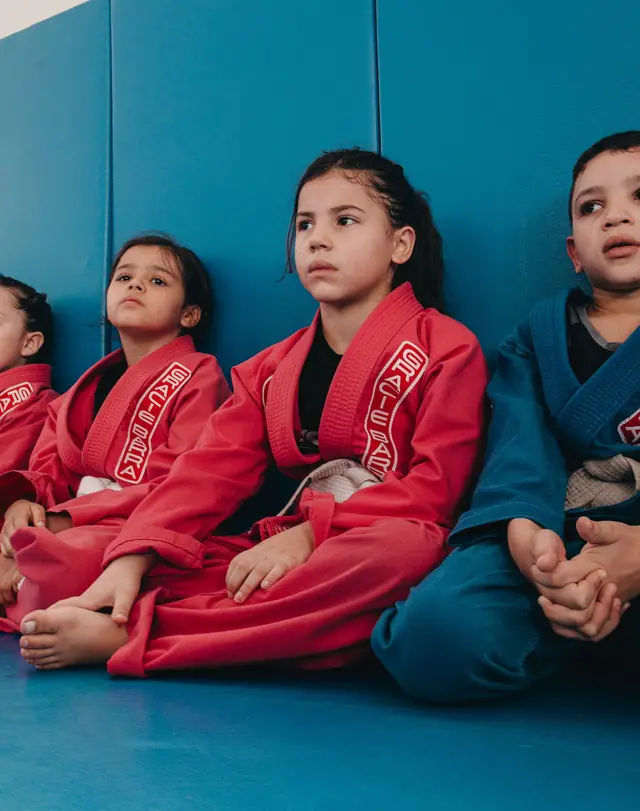 Crianças de kimono sentadas no tatame, atentas à aula