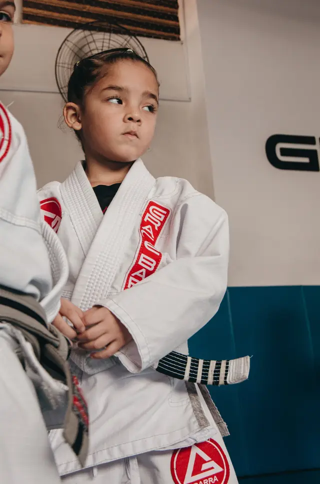 Criança de kimono branco ajustando a faixa antes do treino